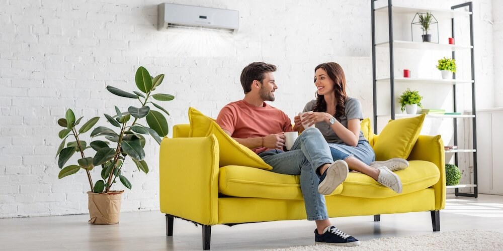 couple sitting on a yellow couch beneath wall-mounted mini split heat pump in living room